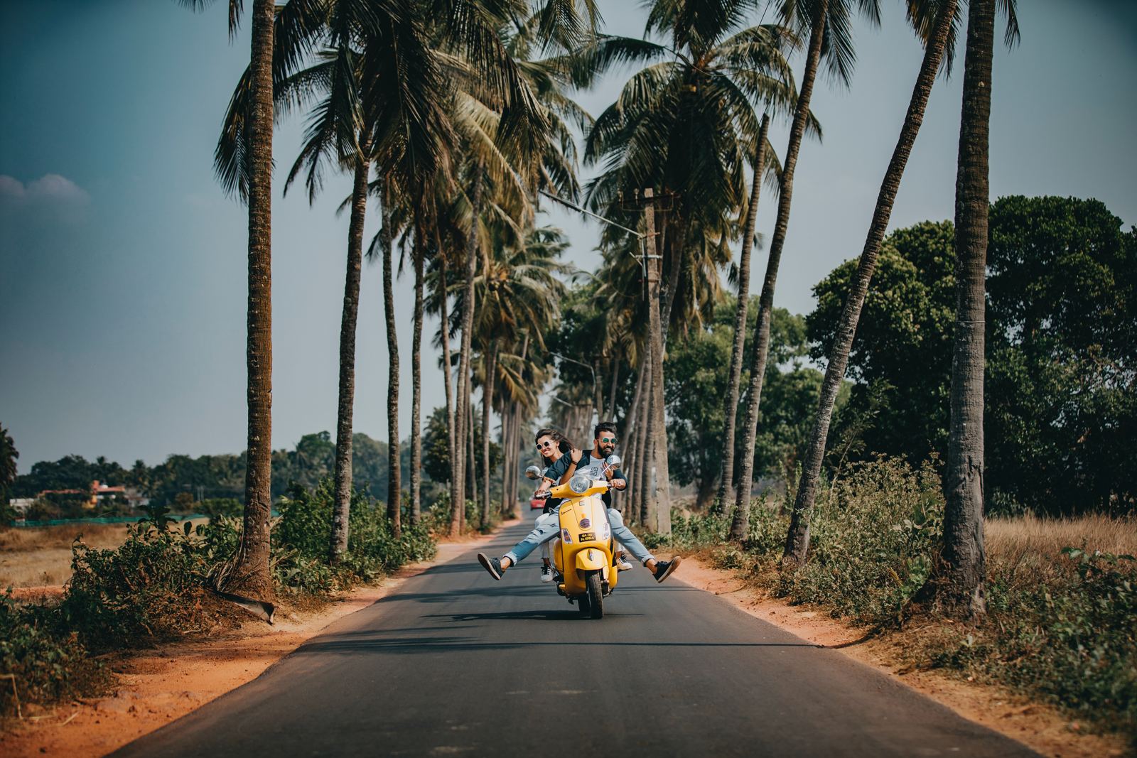 Couple riding a scooter down a palm-lined road